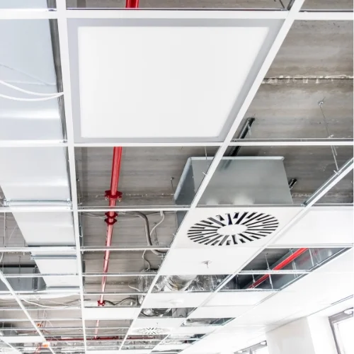 Commercial fire sprinkler pipe installation integrated with HVAC ductwork and lighting systems within an open drop-ceiling grid framework.