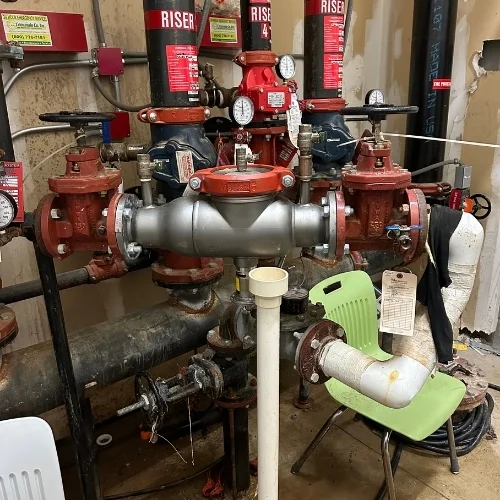 Commercial fire sprinkler system backflow preventer assembly connected to main water risers, with pressure gauges and control valves in a mechanical utility room.