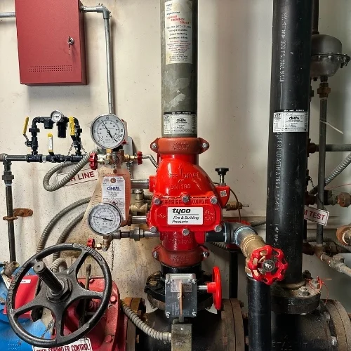 A red Tyco dry pipe valve assembly installed on a fire sprinkler riser system, featuring pressure gauges, an air line, and a control wheel in a mechanical room.
