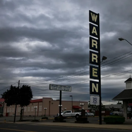 Roadside commercial street signs on a cloudy day in Warren, Ohio, featuring the large vertical "WARREN" sign and local business storefronts.
